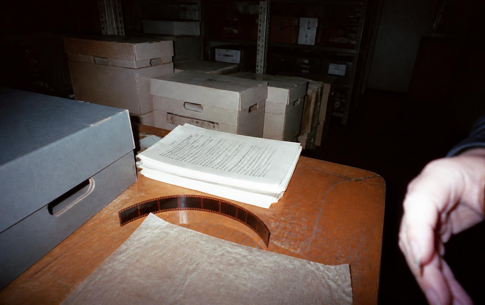 A stack of typewritten pages and a strip of microfilm on a dark desk